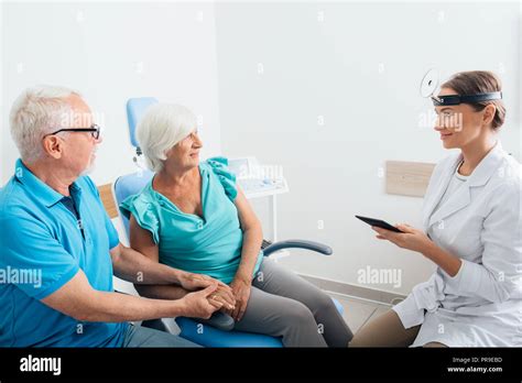 Ent Doctor Talking With Senior Patients In Doctors Office Stock Photo